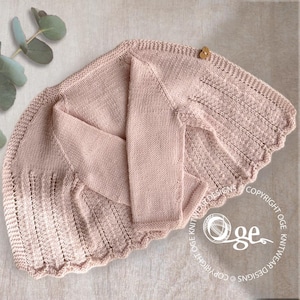 May include: A light pink knitted baby cardigan with a scalloped edge and a single wooden button closure. The sleeves are folded, and the garment is lying flat. The design includes textured knit details.