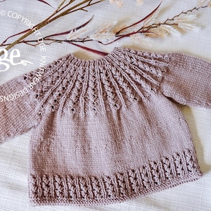 May include: A light brown knitted sweater with a delicate lace pattern around the neckline and hem. The sweater has long sleeves and a round neckline.