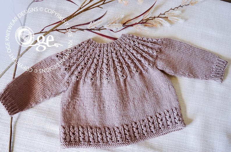 May include: A light brown knitted sweater with a delicate lace pattern around the neckline and hem. The sweater has long sleeves and a round neckline.