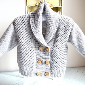 May include: A grey knitted cardigan with a wide collar and three wooden buttons. The cardigan has a textured knit pattern.