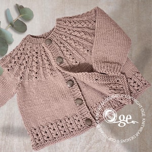 Può includere: Un cardigan di maglia rosa chiaro per neonato con chiusura a bottoni e un delicato motivo a pizzo. Il cardigan ha un collo rotondo e maniche lunghe.