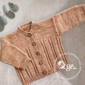 Peut inclure: Cardigan tricoté marron clair avec des boutons en bois. Ce vêtement pour bébé ou enfant présente un col rond et des manches longues. Il comporte des détails côtelés sur le devant et les manches. Le design est de style boutonné.