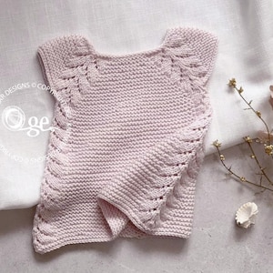 May include: A pale pink knitted sleeveless top with a delicate lace pattern around the neckline and armholes.