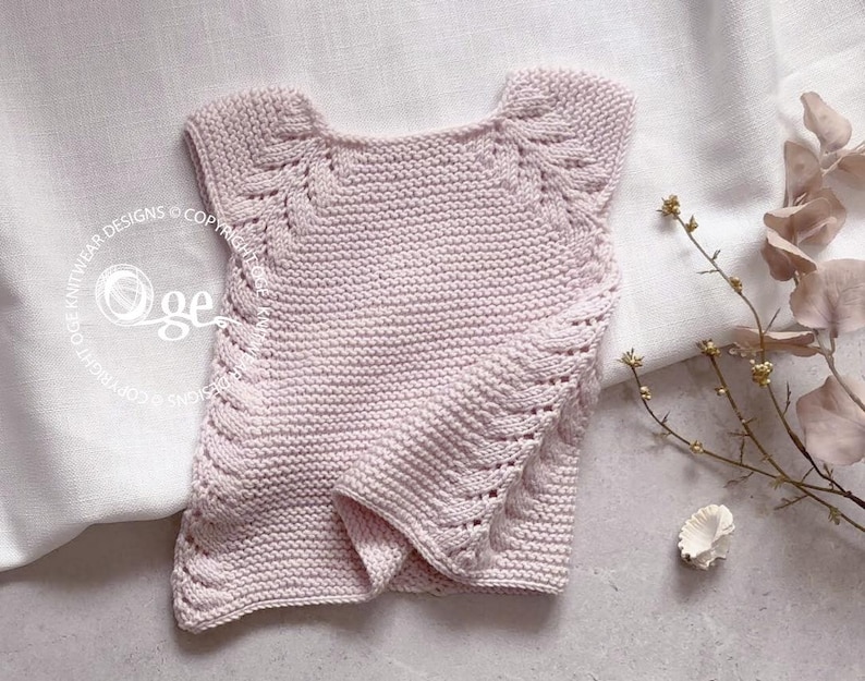 May include: A pale pink knitted sleeveless top with a delicate lace pattern around the neckline and armholes.