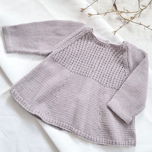 May include: A light gray knitted baby dress with long sleeves and a round neckline. The dress has a textured pattern on the bodice and a simple knit on the skirt.