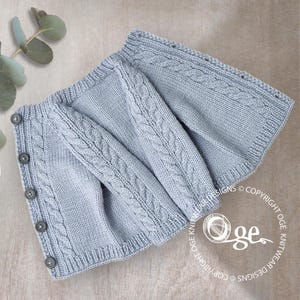 Peut inclure: Un cardigan de bébé tricoté bleu clair avec un motif de torsades sur les manches et le devant. Le cardigan a quatre boutons gris et est plié. Le copyright d'Oge Knitwear Designs est visible.