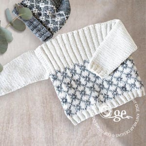 May include: A white and gray knitted sweater with a diamond pattern on the bottom half. The sweater has long sleeves and a crew neck.