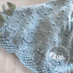 May include: A light blue knitted baby blanket with a textured pattern. The blanket has a scalloped edge and is made with a soft yarn.