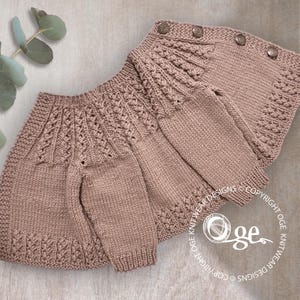 May include: A knitted baby cardigan in a light pink color with a delicate cable stitch pattern. The cardigan has a button closure and is laid flat on a textured surface.