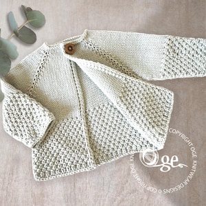 Op de afbeelding: Een lichtgroen gebreid babyvestje met een enkele houten knoopsluiting. Het vestje heeft een textuursteekpatroon op de mouwen en de onderkant, met een gladde brei op het bovenlichaam. Het kledingstuk wordt open getoond.