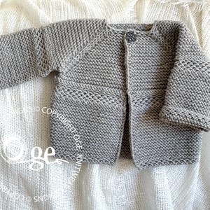 Può includere: Un cardigan in maglia a maniche lunghe grigio chiaro con una trama a legaccio, un singolo bottone decorativo a forma di fiore sullo scollo e una fascia orizzontale con dettagli traforati sul petto e sulle maniche, con filigrana visibile.