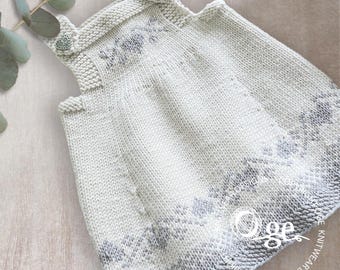 May include: A cream-coloured knitted jumper dress featuring a subtle grey ombre pattern at the hem and chest. The garment has two silver heart-shaped buttons at the shoulder straps and a textured garter stitch finish throughout the bodice.