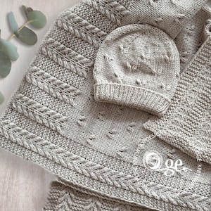 May include: A gray knitted baby blanket and matching hat with a cable knit pattern. The blanket is folded in half and the hat is placed on top of it.