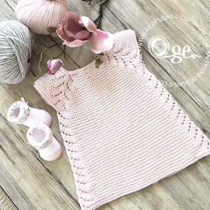 May include: A pink knitted baby dress with a delicate lace pattern around the neckline and hem. The dress is made with a soft yarn and has a simple, classic design.