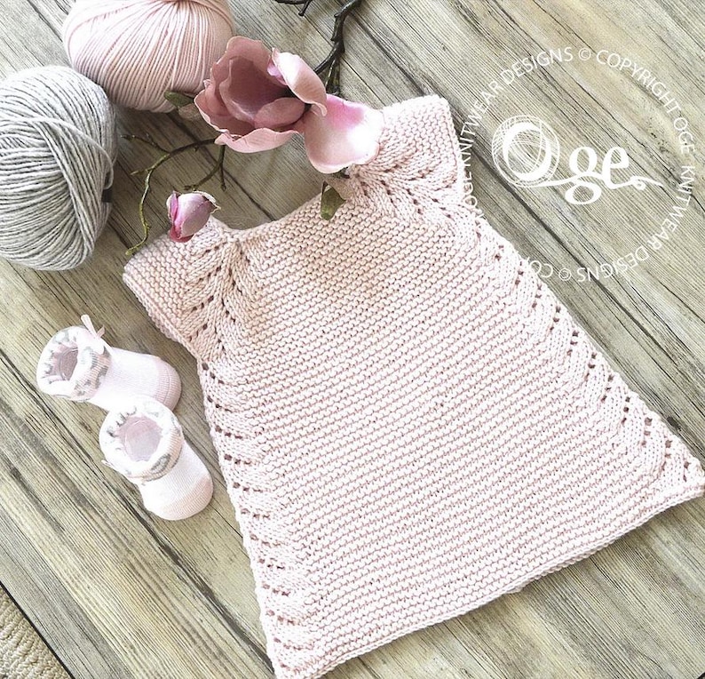 May include: A pink knitted baby dress with a delicate lace pattern around the neckline and hem. The dress is made with a soft yarn and has a simple, classic design.