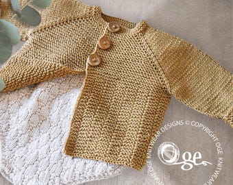 Könnte beinhalten: Ein gestrickter Baby-Cardigan in einem warmen Beigeton mit drei Holzknöpfen. Dazu eine hellgraue, strukturierte Decke. Die Aufnahme zeigt eine Draufsicht, die die weichen Texturen der Strickwaren hervorhebt.