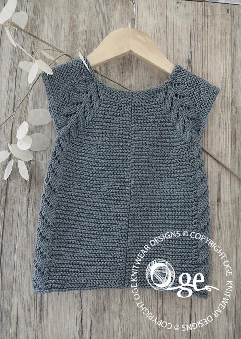May include: A gray knitted sleeveless top with a lace pattern around the neckline and armholes. The top is hanging on a wooden hanger against a woodgrain background.