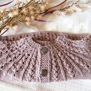 May include: A mauve knitted cardigan with a button closure and a delicate lace pattern. The cardigan is folded in half and laid on a white surface.