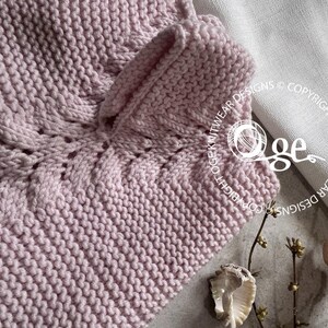 May include: A close-up of a pink knitted fabric with a cable stitch pattern. The fabric is soft and textured, and the stitch pattern creates a subtle, elegant design.