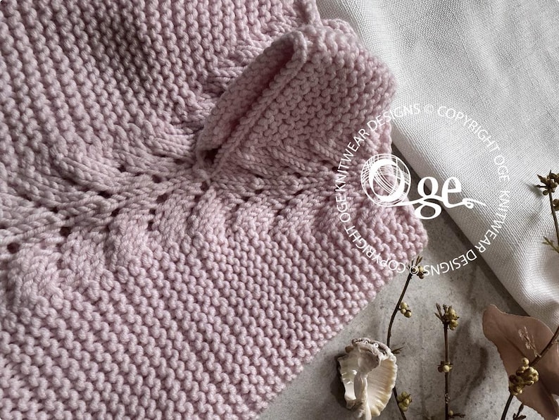 May include: A close-up of a pink knitted fabric with a cable stitch pattern. The fabric is soft and textured, and the stitch pattern creates a subtle, elegant design.