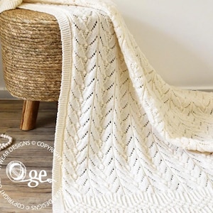 May include: A white crocheted throw blanket with a chevron pattern. The blanket is draped over a woven stool.