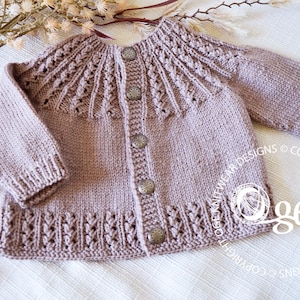 May include: A light brown knitted baby cardigan with a button closure and a delicate lace pattern. The cardigan has a round neckline and long sleeves.