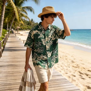 May include: A short-sleeved button-down shirt in dark green featuring a cream-colored tropical print of palm trees and hibiscus flowers, paired with beige shorts, a straw fedora hat, and a beige and white striped towel held in one hand.