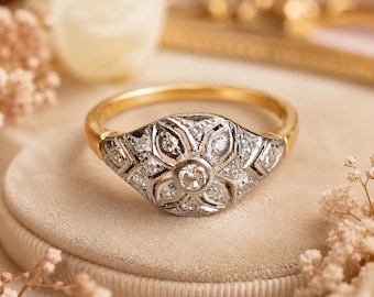 May include: A gold ring featuring a central circular diamond surrounded by a floral-shaped setting of smaller diamonds in a silver-toned metal. The band is smooth and gold, while the decorative head displays intricate metalwork and multiple stones.