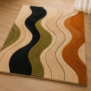 May include: A rectangular area rug featuring a textured, wavy pattern with alternating bands of cream, olive green, black, and burnt orange. The design consists of raised, curved sections that create a sense of depth across the surface of the rug.