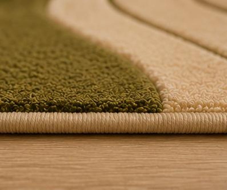 May include: A textured rug featuring alternating wavy bands of olive green and cream. The edge of the rug is finished with a tightly bound cream-colored yarn border that runs horizontally across the bottom of the frame.