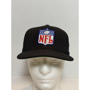 Op de afbeelding: Een zwarte honkbalpet met een geborduurd NFL-logo op de voorzijde. Het logo bestaat uit een blauw bovengedeelte met witte sterren en een witte football, en een wit benedengedeelte met de rode letters NFL omlijnd in het blauw.