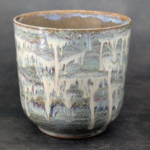 May include: A handcrafted ceramic bowl with a unique glaze. The bowl features a blend of blue, white, and brown hues, with a dripped glaze effect. The interior is a warm brown, and the exterior has a textured appearance. This decorative bowl is ideal for serving or display.