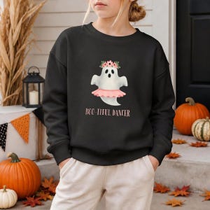 May include: A black long-sleeve sweatshirt featuring a graphic of a white ghost wearing a pink tutu and a floral crown. The text "BOO-TIFUL DANCER" is printed in pink lettering below the ghost illustration. The garment has a crew neckline.