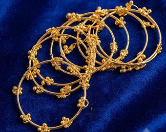 May include: A set of gold-toned metal bangles featuring a thin circular band design adorned with small, evenly spaced clusters of tiny spherical beads. The bangles are arranged in an overlapping stack, showcasing the metallic finish and texture.