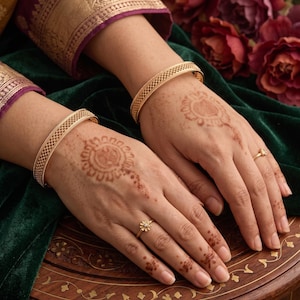 May include: Two gold bangles featuring a fine, intricate lattice pattern. Each bangle is a solid, polished gold band with a consistent width and a textured, cross-hatched design across the outer surface, providing a uniform and detailed appearance.