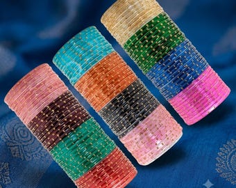 May include: Three stacks of cylindrical bangles featuring a translucent finish with embedded gold-colored glitter accents. The bangles are arranged in various colors including pink, dark brown, green, orange, black, blue, and beige.