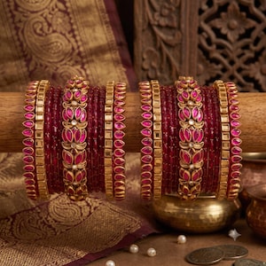 Puede incluir: Dos juegos de brazaletes con anillos de vidrio translúcido rojo oscuro intercalados con bandas de metal dorado. Las bandas centrales presentan un patrón floral repetitivo de piedras rosas en forma de lágrima engastadas en metal.