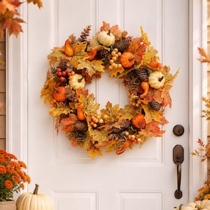 May include: A circular autumn wreath featuring a mix of orange and yellow maple leaves, small white and orange pumpkins, brown pinecones, and clusters of red and yellow berries. The wreath is arranged in a dense, layered circular pattern.