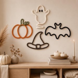 May include: A set of four wall-mounted yarn art pieces featuring a bright orange pumpkin with a green stem, a white ghost with black eyes, a black bat with outstretched wings, and a dark brown witch hat with a buckle detail.