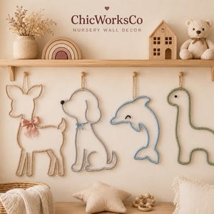 May include: Four wall-mounted animal silhouettes made of wrapped cord, including a deer with a pink bow, a dog, a dolphin, and a dinosaur. The wall decor is displayed below a wooden shelf holding a vase, a rainbow, a house, and a teddy bear.