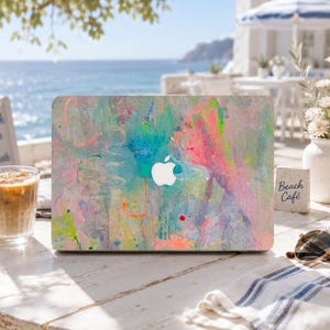 Può includere: Una skin per laptop con un design astratto a schizzi di vernice in tonalità vivaci di rosa, blu, giallo e verde. Il design copre il coperchio esterno del laptop e presenta un ritaglio centrale per il logo Apple bianco.