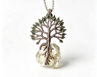 May include: A pendant necklace featuring a tree of life design crafted from brown and olive green thread. The tree roots wrap around a translucent, pale yellow, multifaceted crystal stone. The pendant hangs from a matching braided cord.