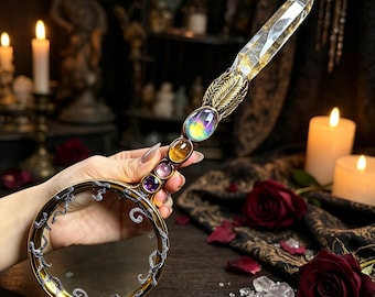 May include: A handheld magnifying glass featuring a circular frame with silver vine-like filigree. The handle is adorned with a row of four colorful cabochon gemstones and topped with a long, clear, faceted crystal point in a gold-toned setting.