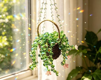 May include: A hanging basket made of dark brown woven material containing a trailing plant crafted from translucent green glass beads. The plant features small pink and white glass flowers and is suspended by clear beaded chains.