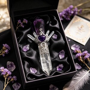 Puede incluir: Una varita de cristal de cuarzo transparente y amatista con una piedra central de amatista en forma de coraz&oacute;n engastada en metal plateado con filigranas, presentada en una caja negra forrada de sat&eacute;n negro con piedras de amatista.