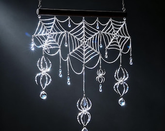 May include: A decorative wall hanging featuring a silver-toned spiderweb pattern suspended from a horizontal bar. The web is adorned with multiple dangling crystal-like spiders and faceted clear beads that catch the light, creating a sparkling effect.
