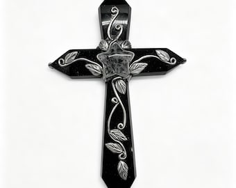 May include: A black cross made of polished stone with a smooth, reflective surface. The cross is adorned with silver-toned metal wirework featuring swirling vine patterns and small leaves. A clear, star-shaped crystal is centered at the intersection.
