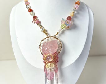 May include: A necklace featuring a large, clear, pointed crystal pendant topped with a rough rose quartz stone, framed by gold wire. The pendant is accented with pink leaf-shaped charms and a round pink bead. The chain consists of multi-colored beads.