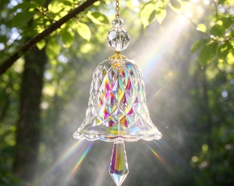 May include: A clear glass bell ornament featuring a diamond-cut pattern with an iridescent finish. The bell hangs from a gold-toned chain and includes a faceted crystal bead at the top and a pointed, multi-colored crystal prism clapper.