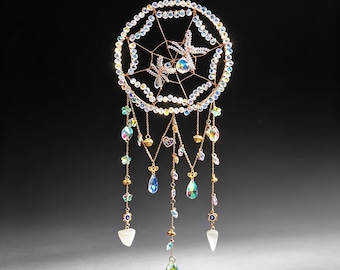 May include: A circular hanging ornament featuring a wire web frame adorned with iridescent beads and two dragonfly figures. Multiple gold-toned chains dangle from the bottom, decorated with small flower-shaped beads, heart charms, and various clear crystal pendants.